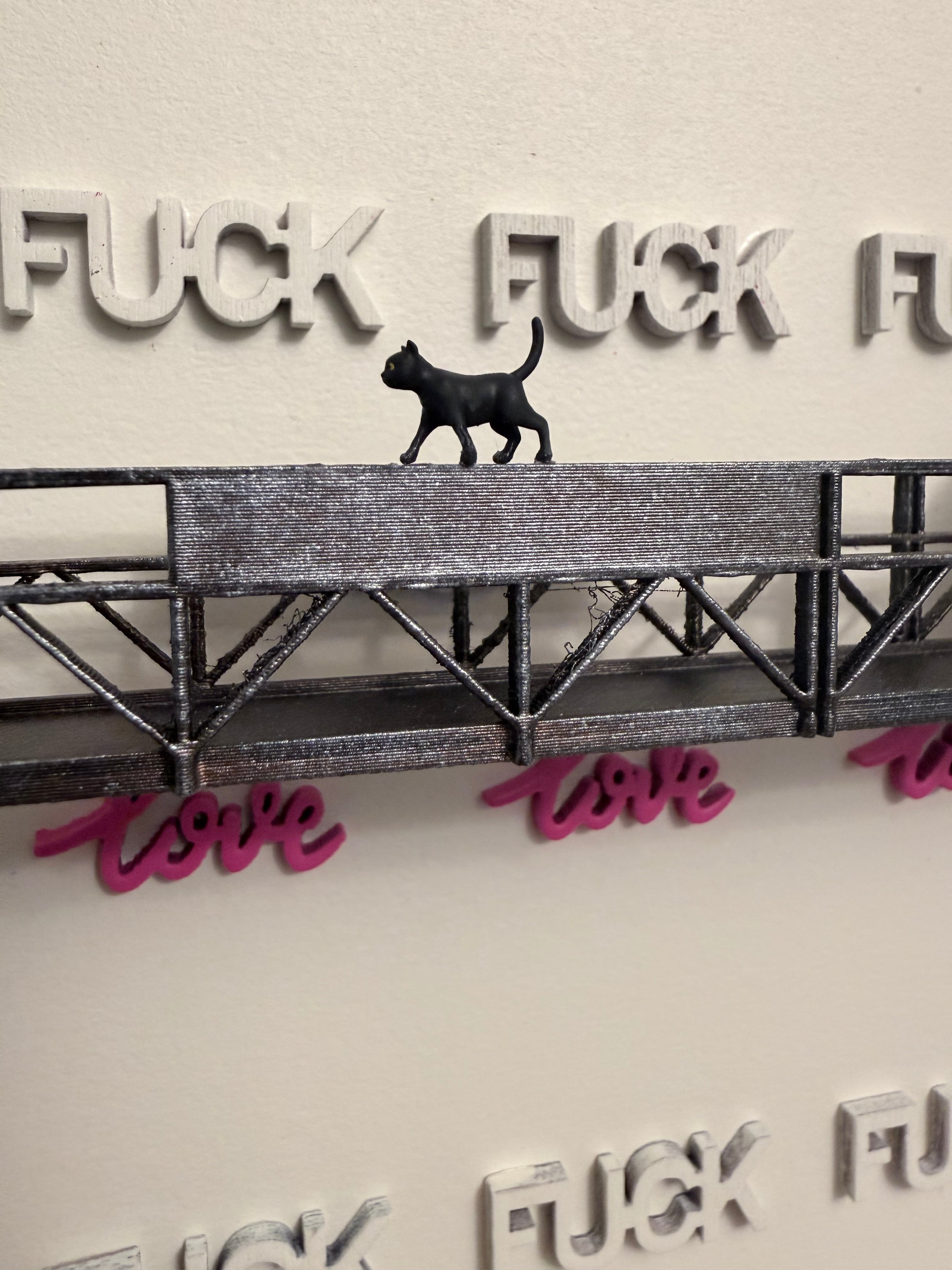 Miniature figurine of a black cat walking on a platform. Background, we can see LOVE and FUCK words aligned perfectly. 