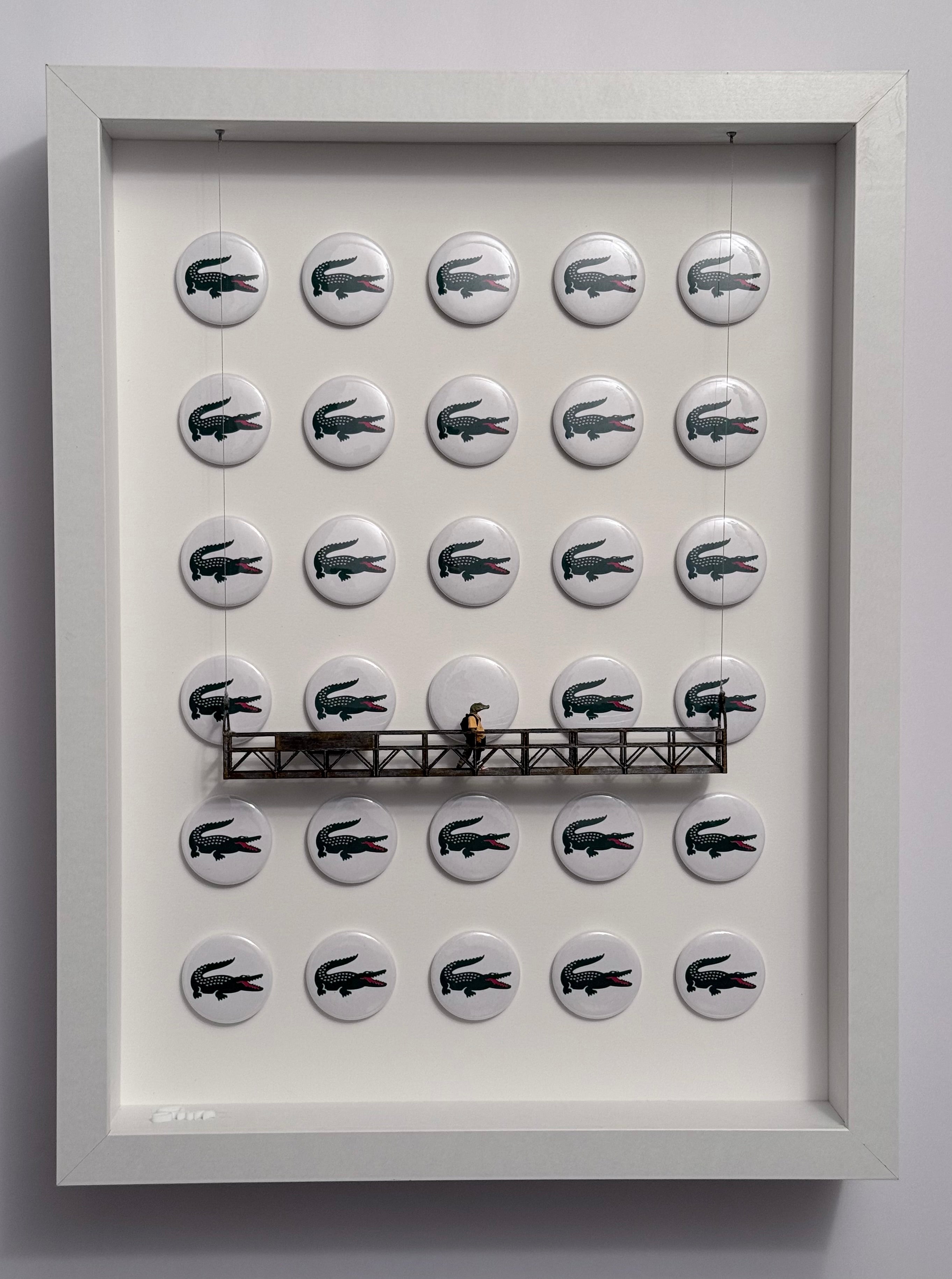 Shadow box artwork with buttons featuring a crocodile logo and crocodile miniature figurine wearing sneakers and a hoodie on a platform.