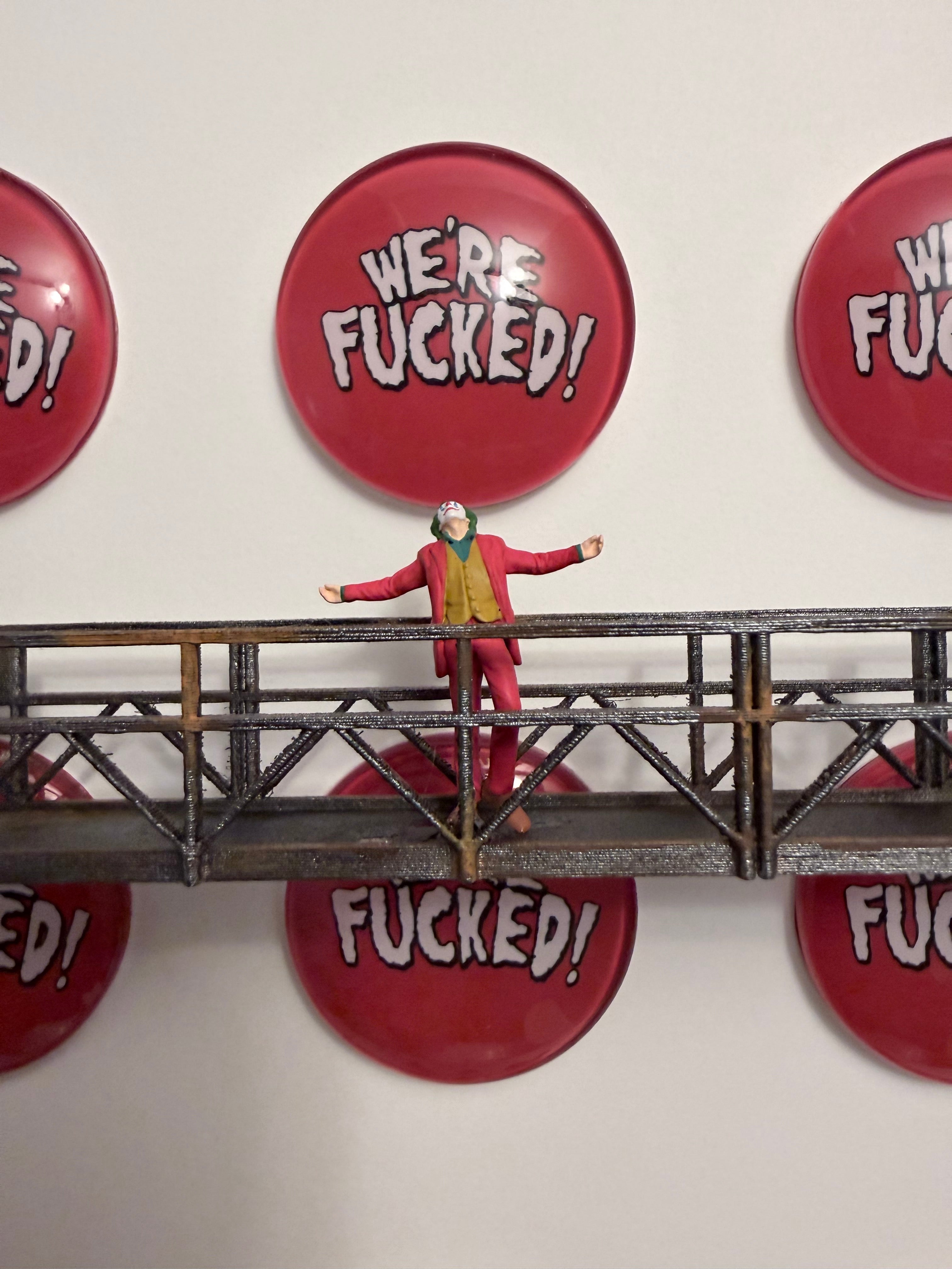 Red buttons with profanity on a white background with a metal platform with a miniature figurine of the Joker.