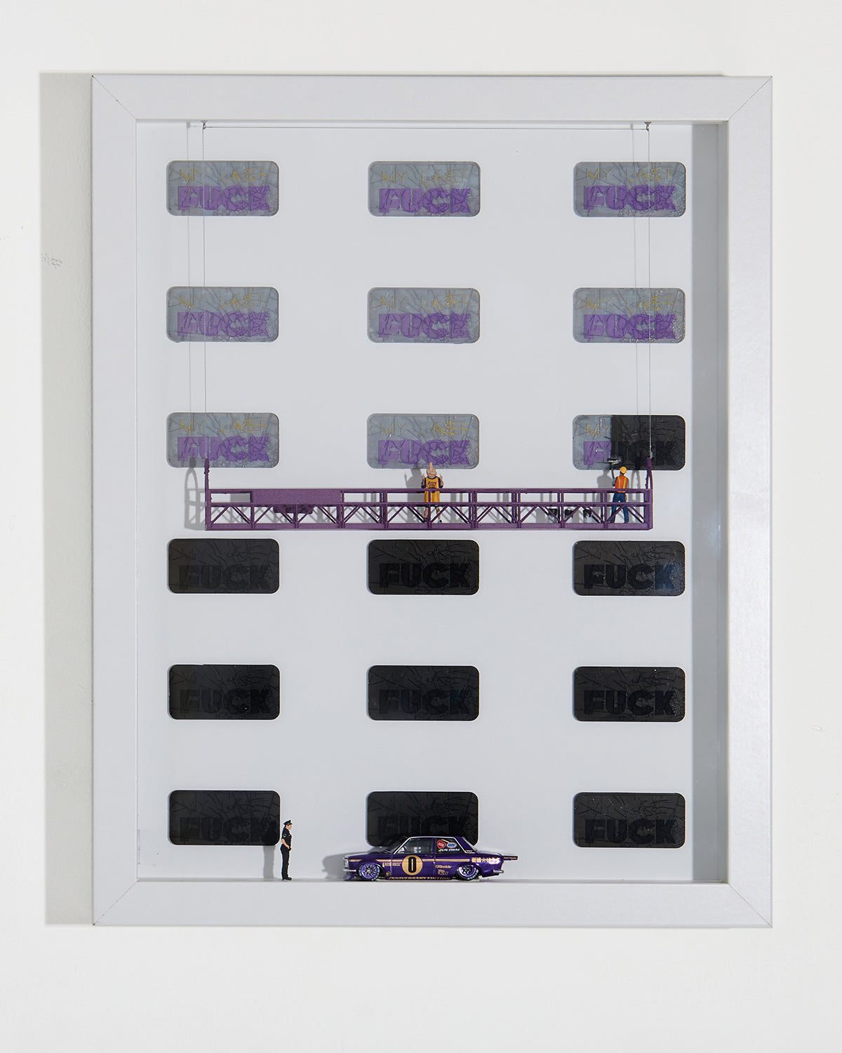 Shadow box artwork displaying the word FUCK multiple time. A miniature figurine covers the words with black paint while another miniature figurine is showing both middle fingers. they are both standing on a platform.