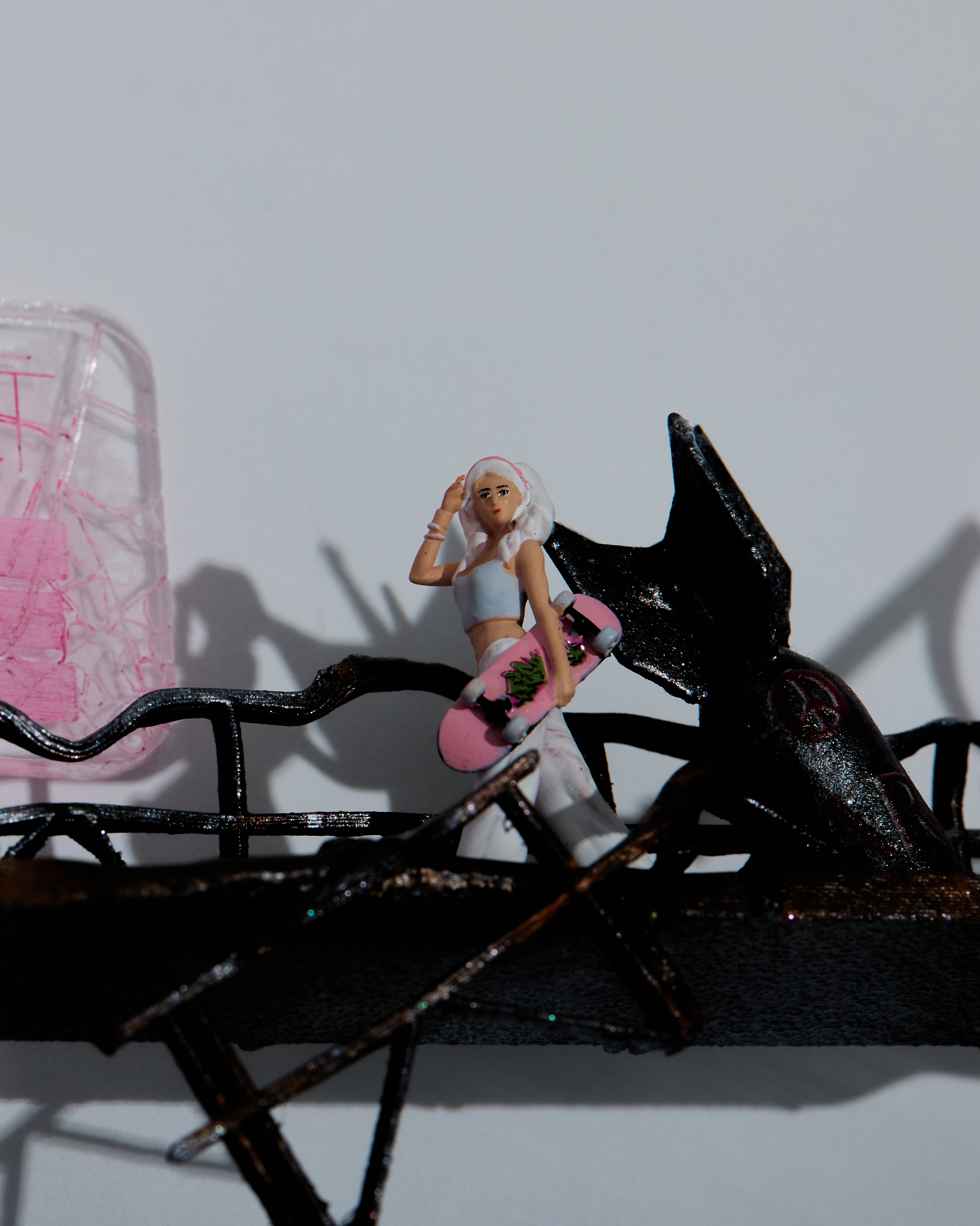 Miniature figurine of a girl walking on a destroy platform with bombs. She is holding a skateboard. Shadow box artwork with white background and frame. 