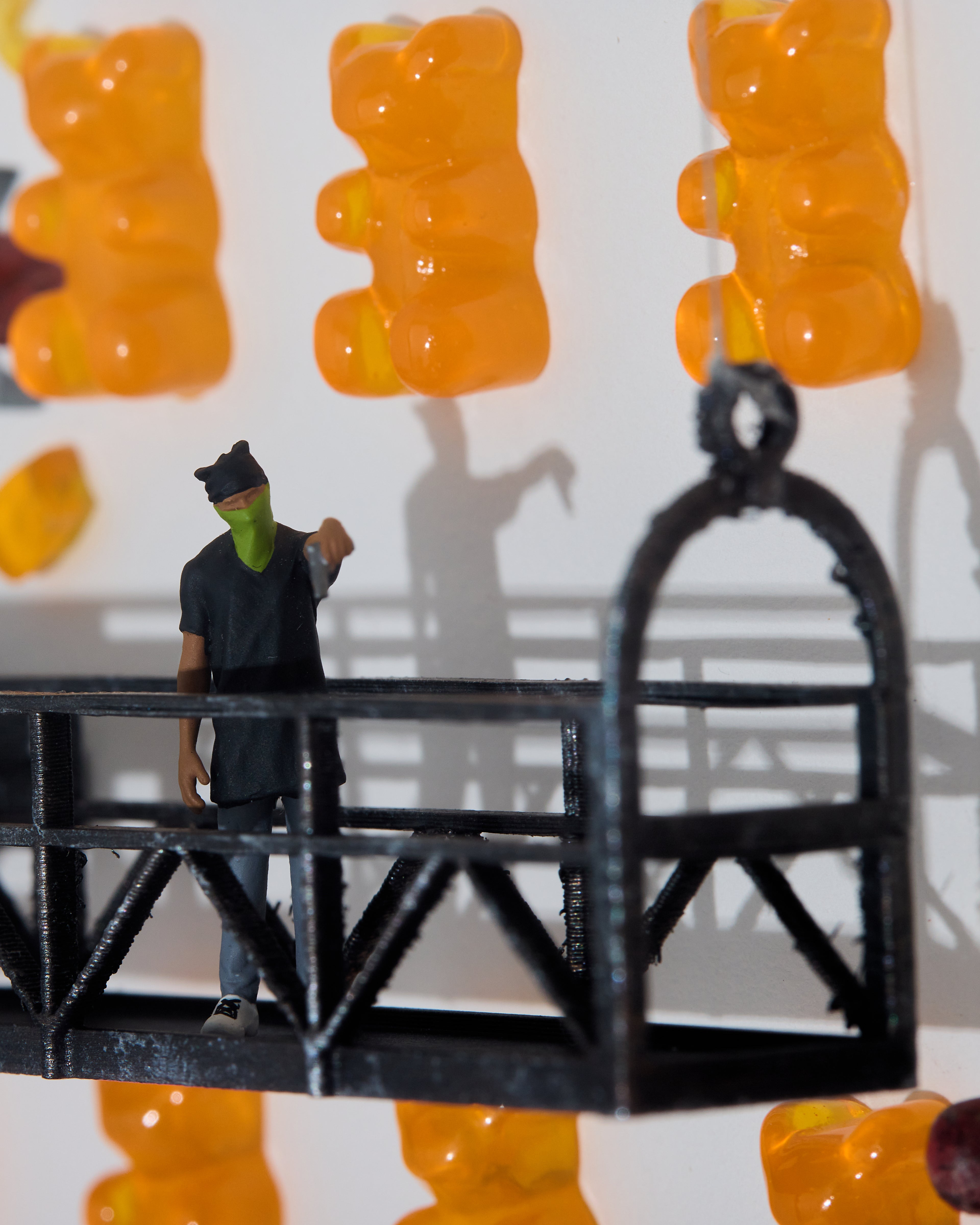 miniature figurine with a green mask and a gun standing on a black platform with gummy bears in the background.