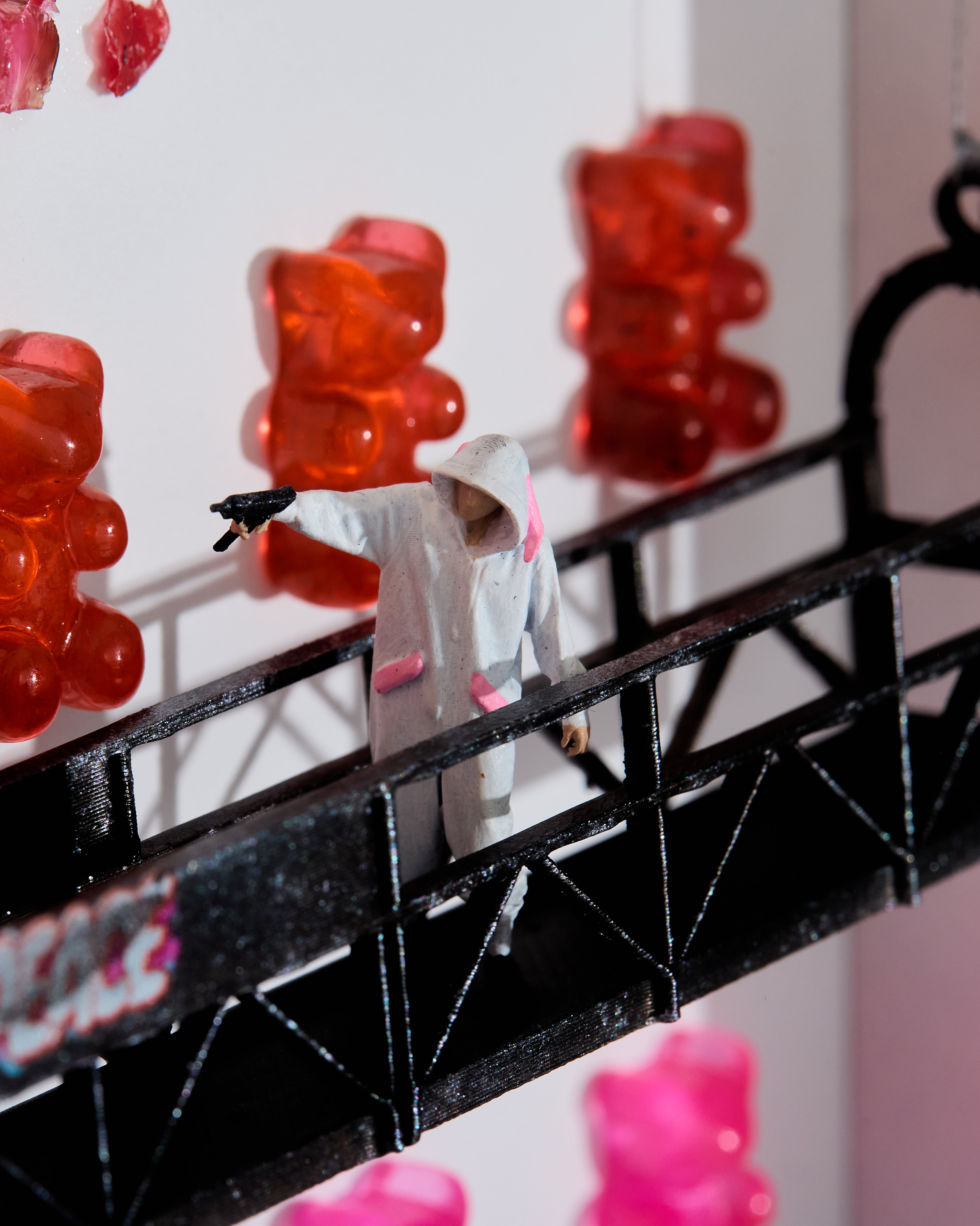 Miniature figurine in his pajamas and holding a gun standing on a black platform with red and pink gummy bear in the background.