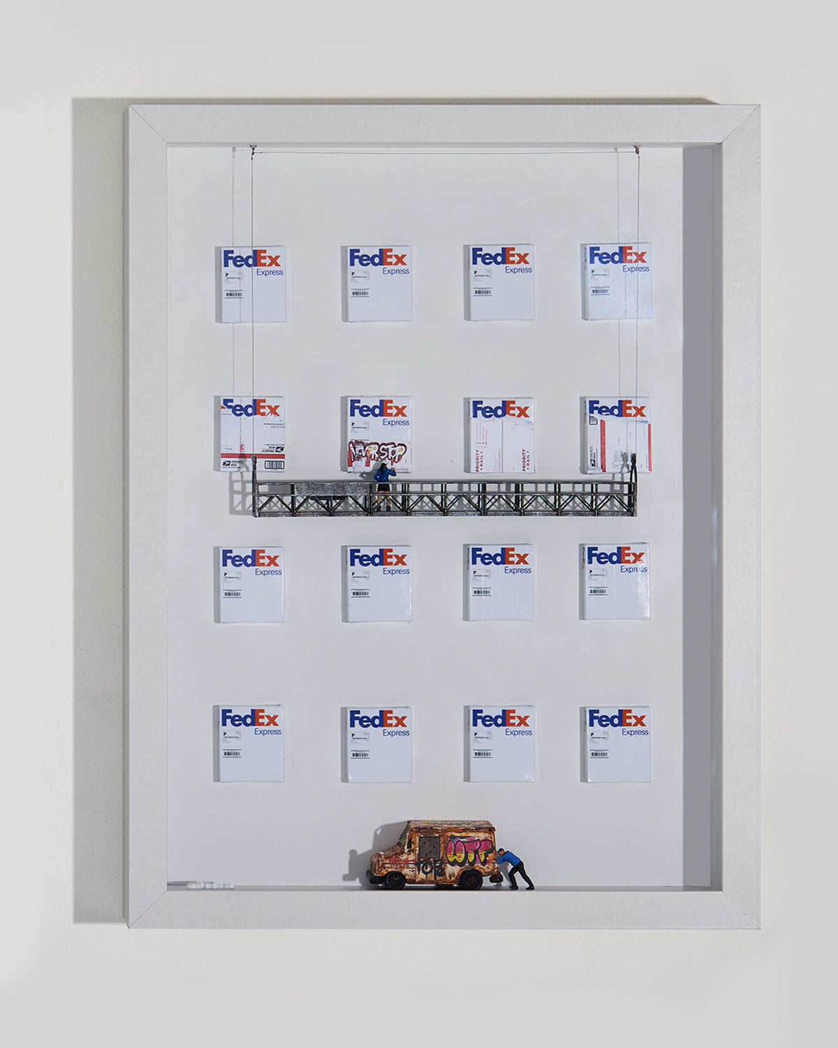 Shadow box with multiple FedEx logos and a USPS truck, old and full of graffiti. A miniature figurine is pushing it,  on a white background