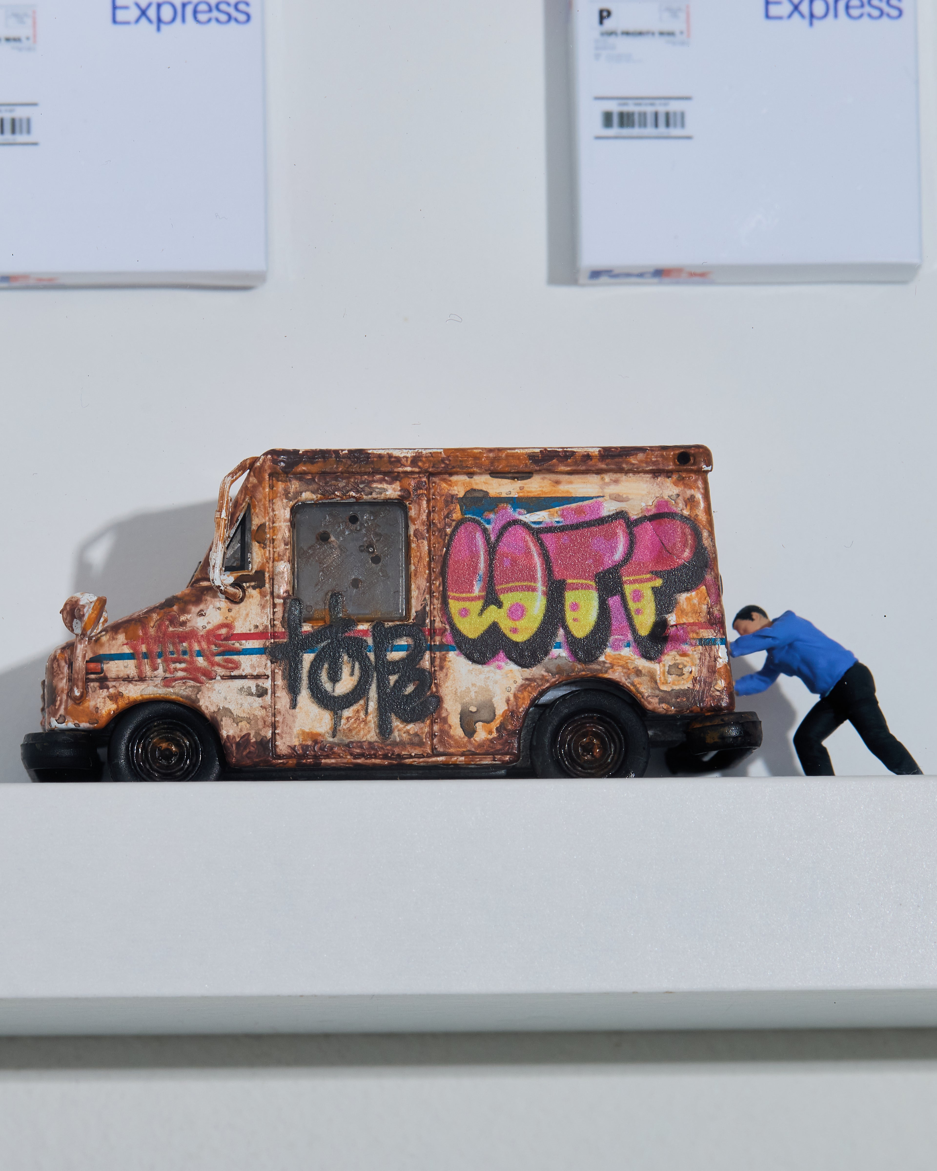 USPS rusted van with graffiti and a miniature figurine pushing it. 