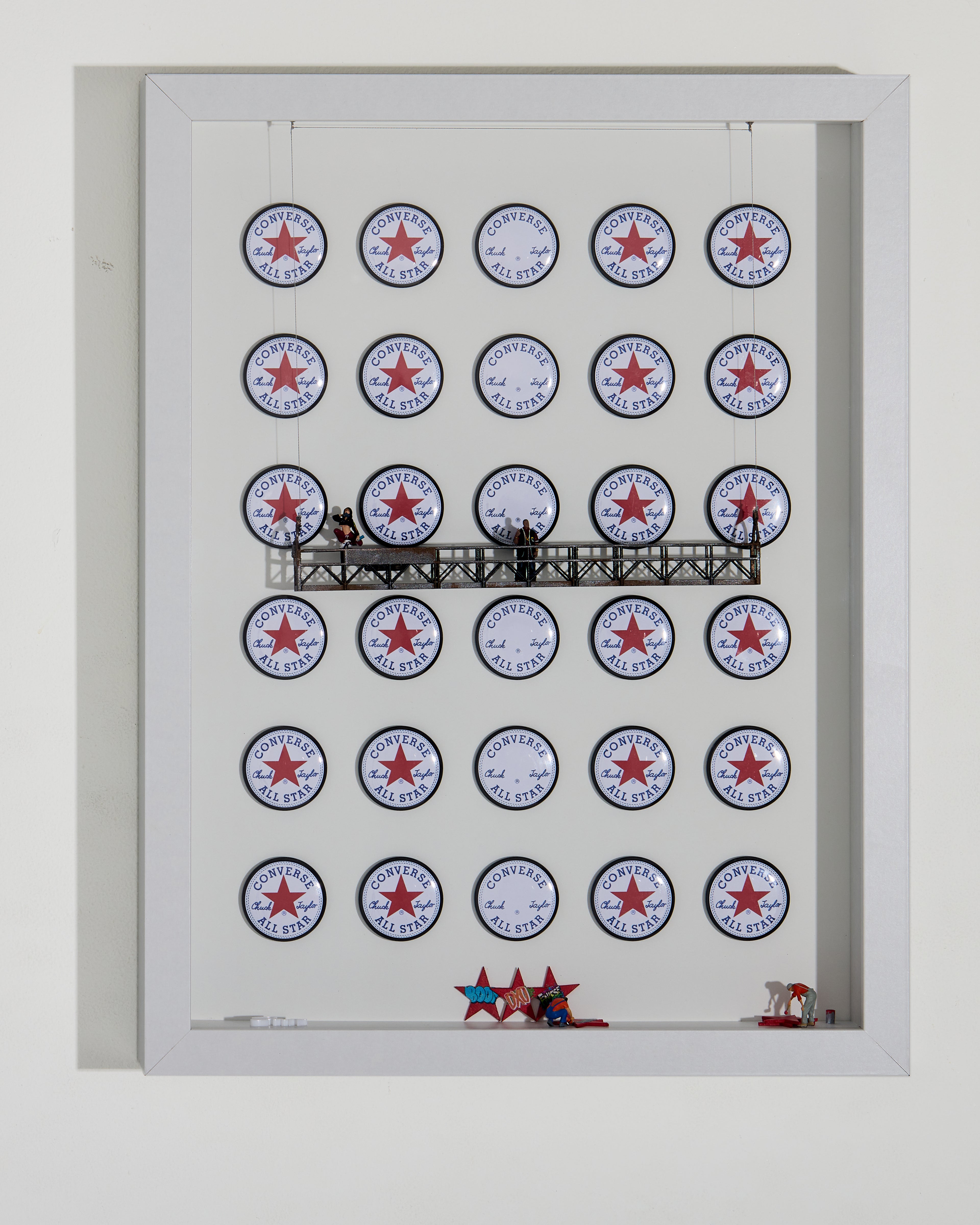 Shadow box artwork with Converse logo pattern on a white background, with miniature figurines on a platform.