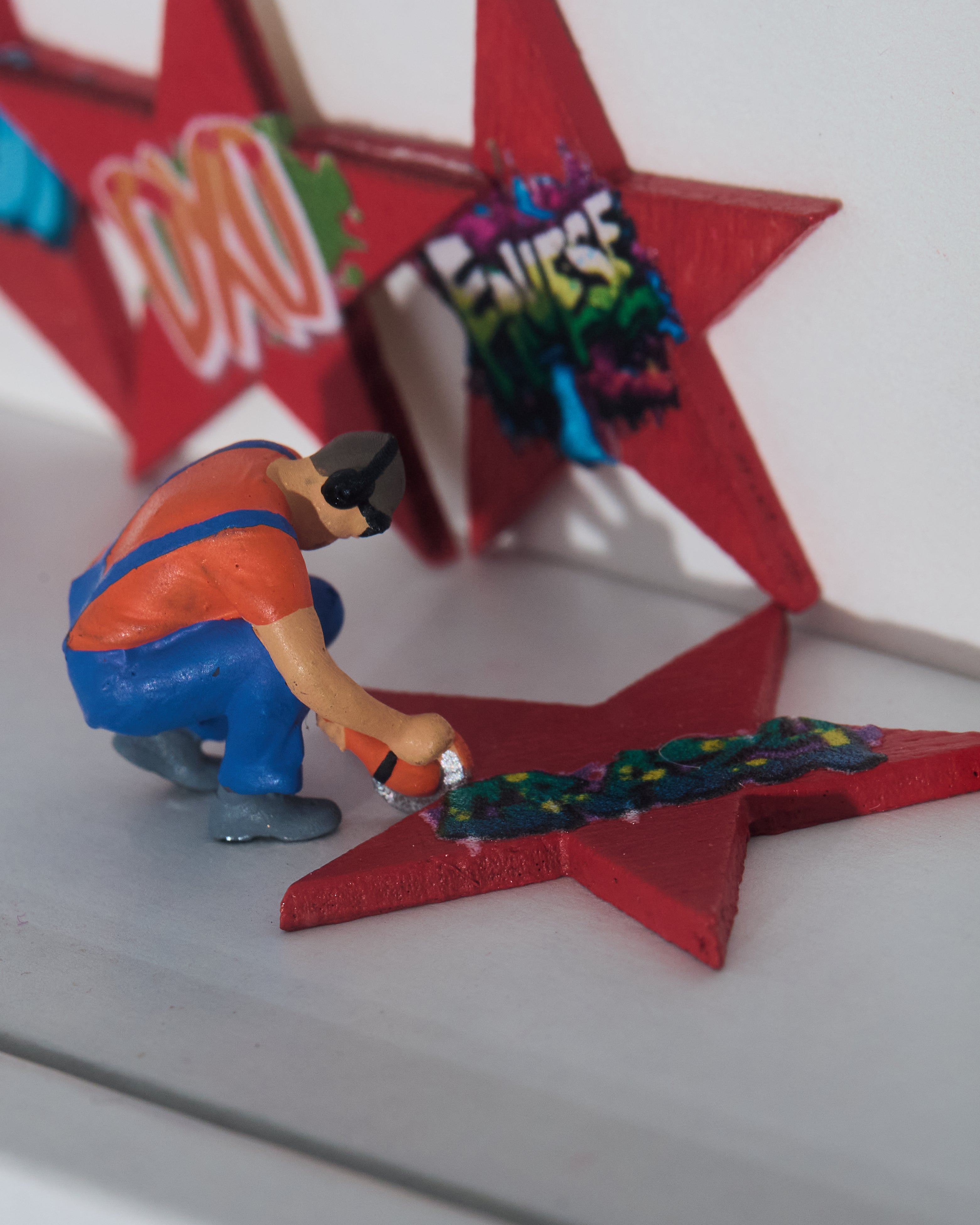Miniature figurine painting a red star-shaped object with colorful text in the background.
