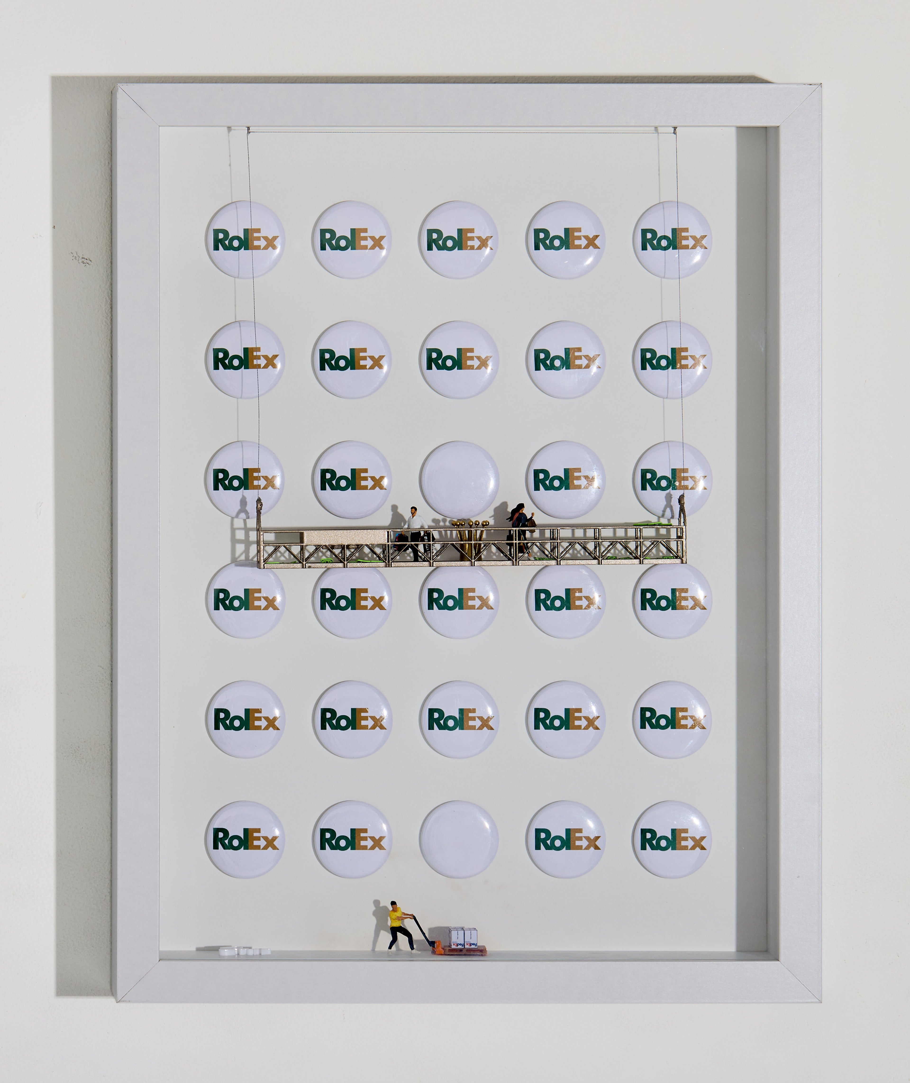 Miniature figurines inside a shadow box stand before a repetitive background inspired by luxury and speed. The scene critiques the link between wealth, time, and privilege — how some can afford to play while others race to catch up. A reflection on how branding shapes value and perception.