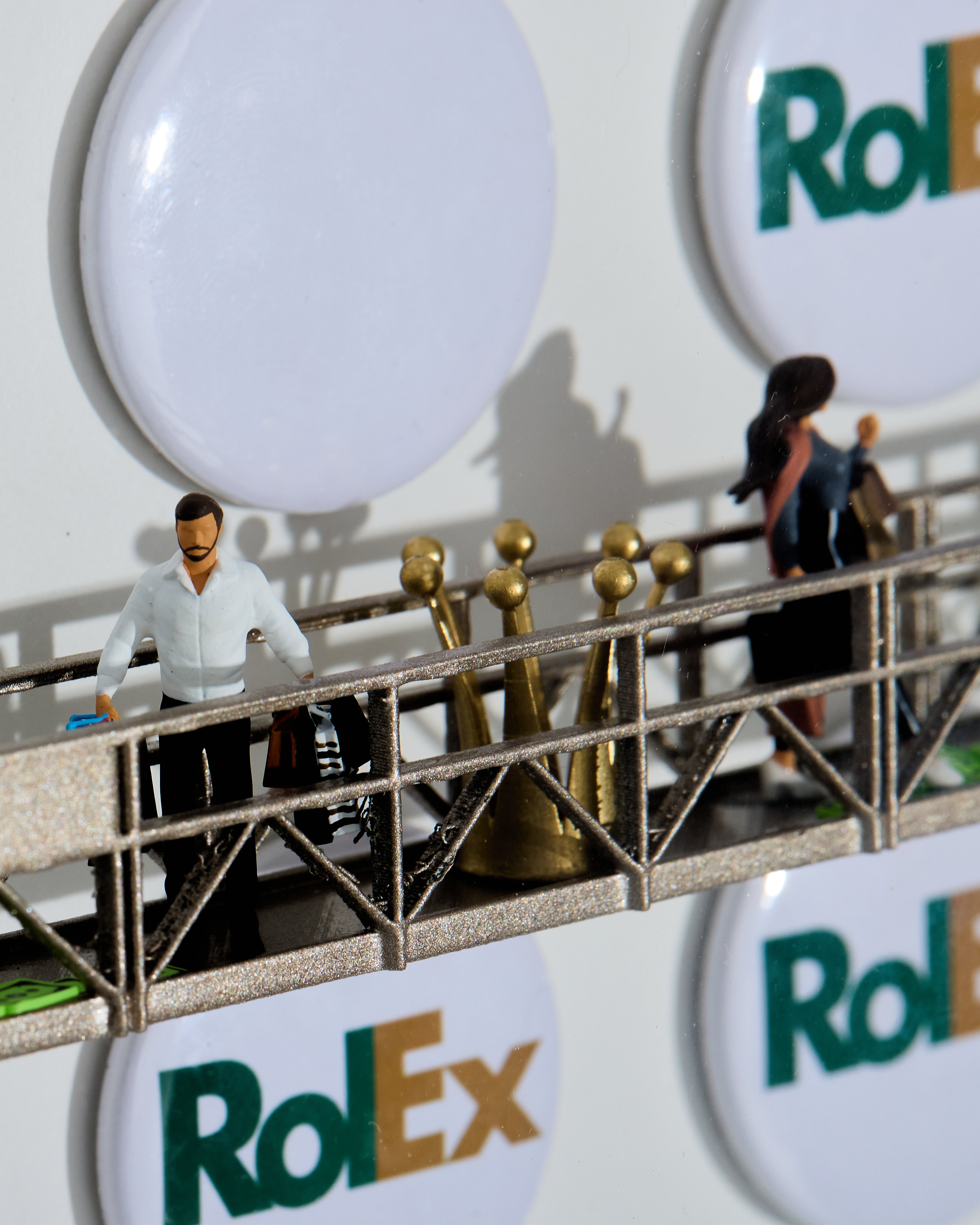 Model of a bridge with small figures on top, set against luxury logos.