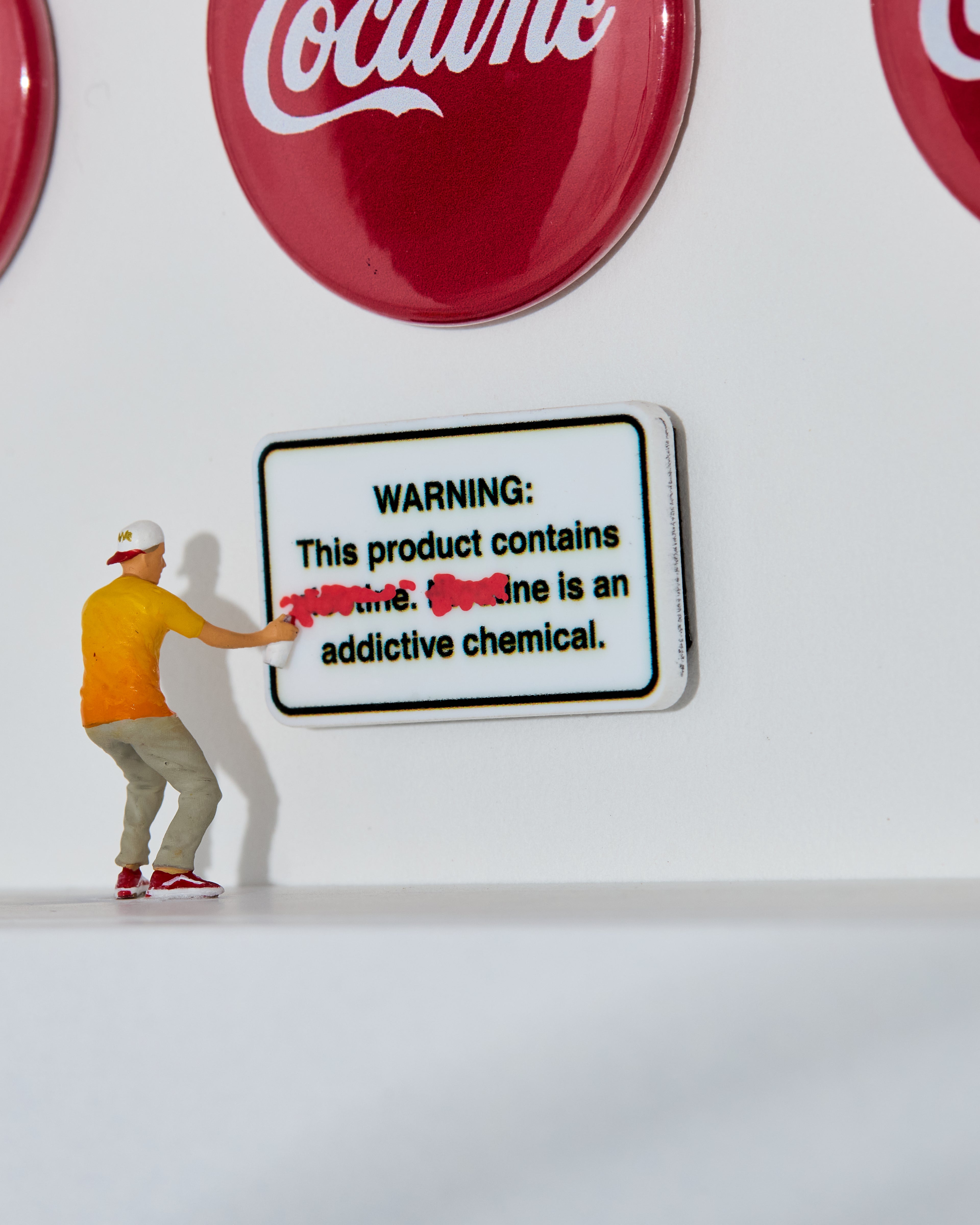 Miniature figurine painting a warning sign in front of Cocaine logos