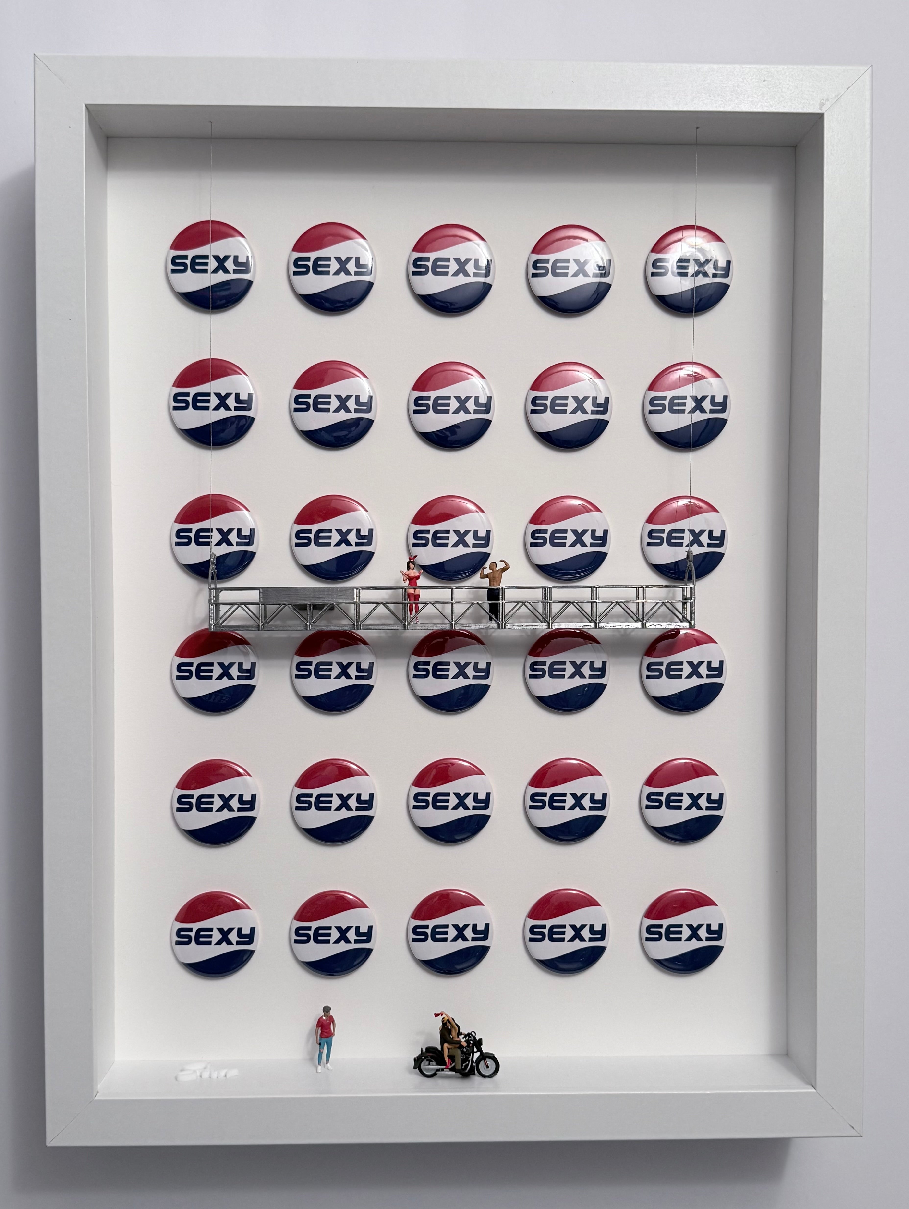 Shadow box artwork displaying 'SEXY' buttons with a miniature model of a motorcycle and people . Silver platform.